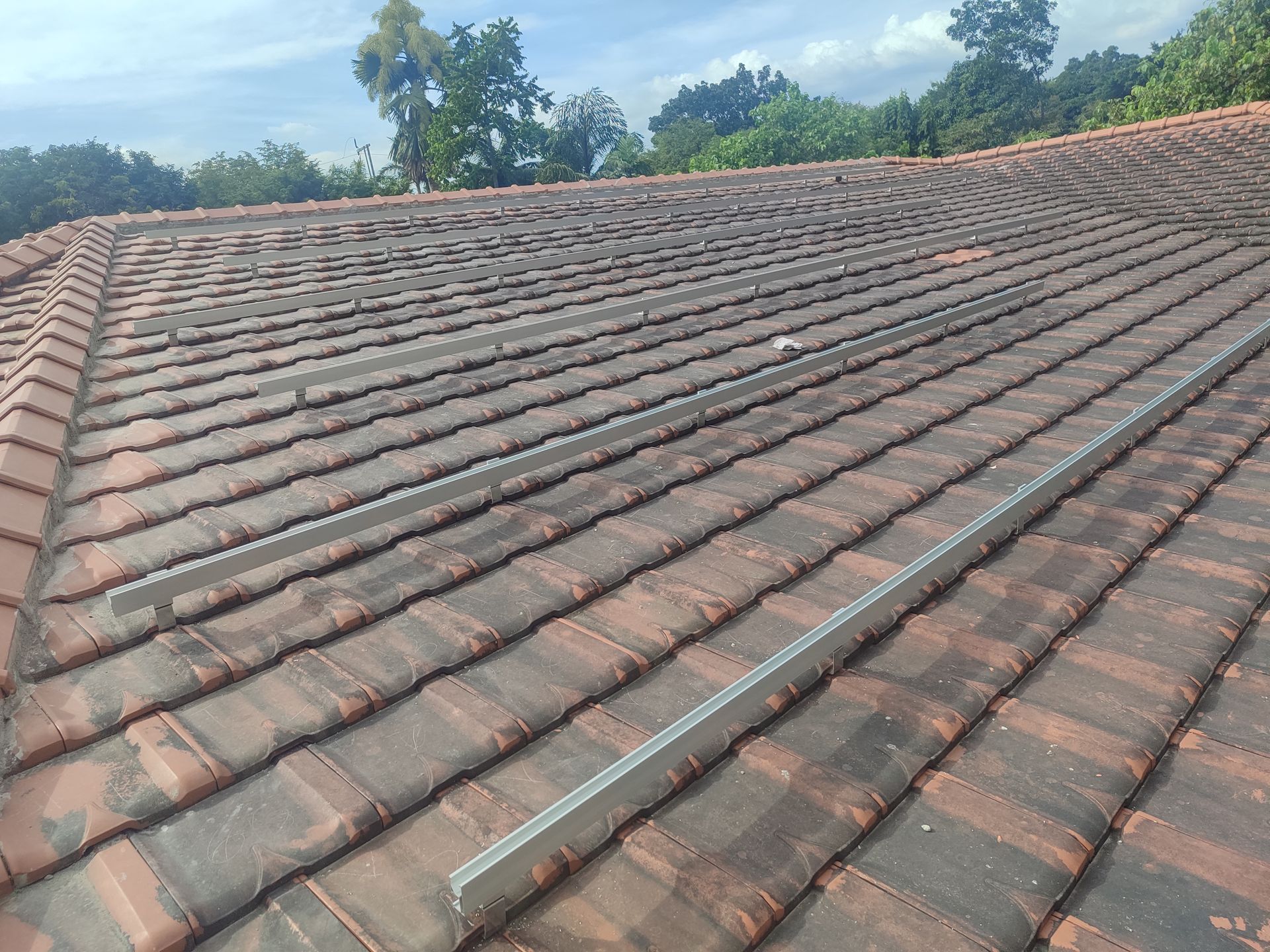 Mounting rails installed on a tiled roof before solar panel placement, showing under-tile hook fixings