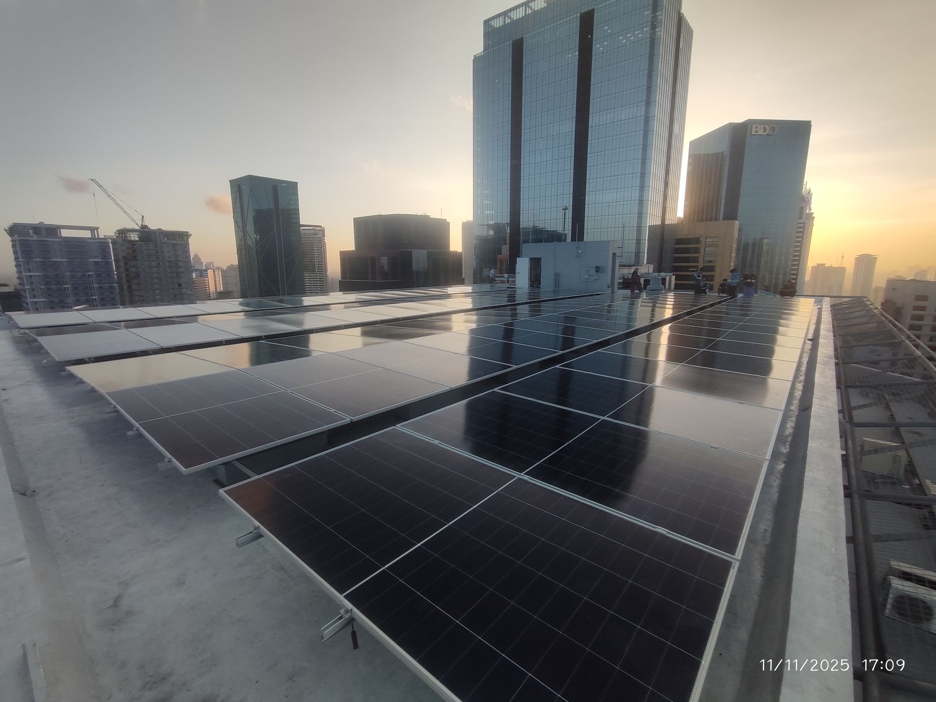 Rooftop solar array on a commercial building with high-rise towers behind, Metro Manila